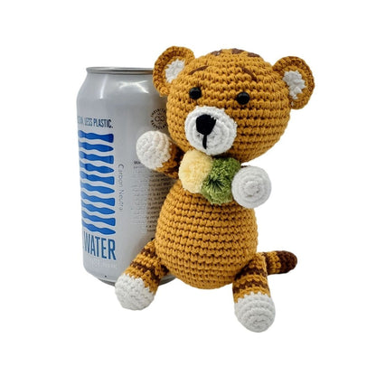 Crocheted tiger toy next to a can of water can on a white background