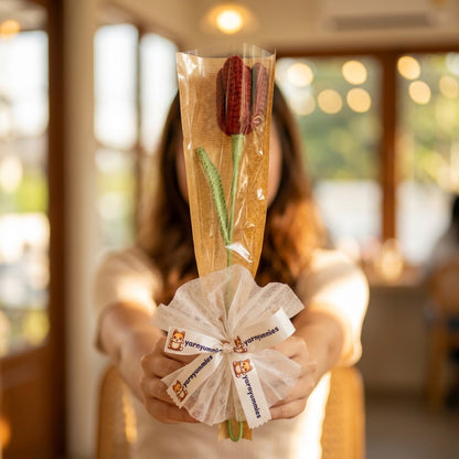 Person holding a bouquet of crocheted  red tulip wrapped in cellophane with decorative ribbons.