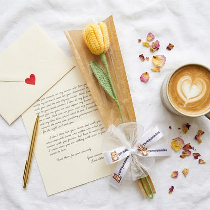 Crocheted tulip, letter, pen, and cup of coffee on a textured surface