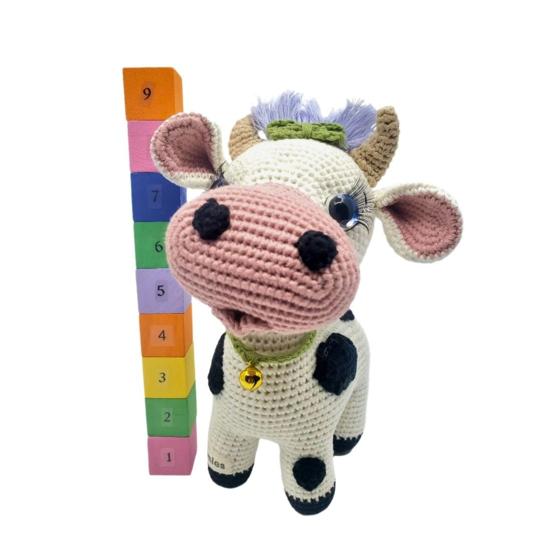 Crocheted cow plushie with a colorful height chart on a white background
