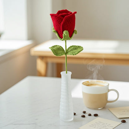 Knitted red rose in a white vase on a table with a coffee cup and beans.