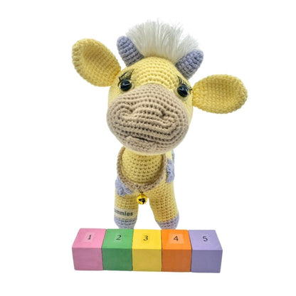 Crocheted yellow cow plushie with colorful blocks on a white background