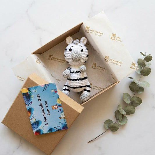 Crocheted zebra toy in a box with a card on a marble surface