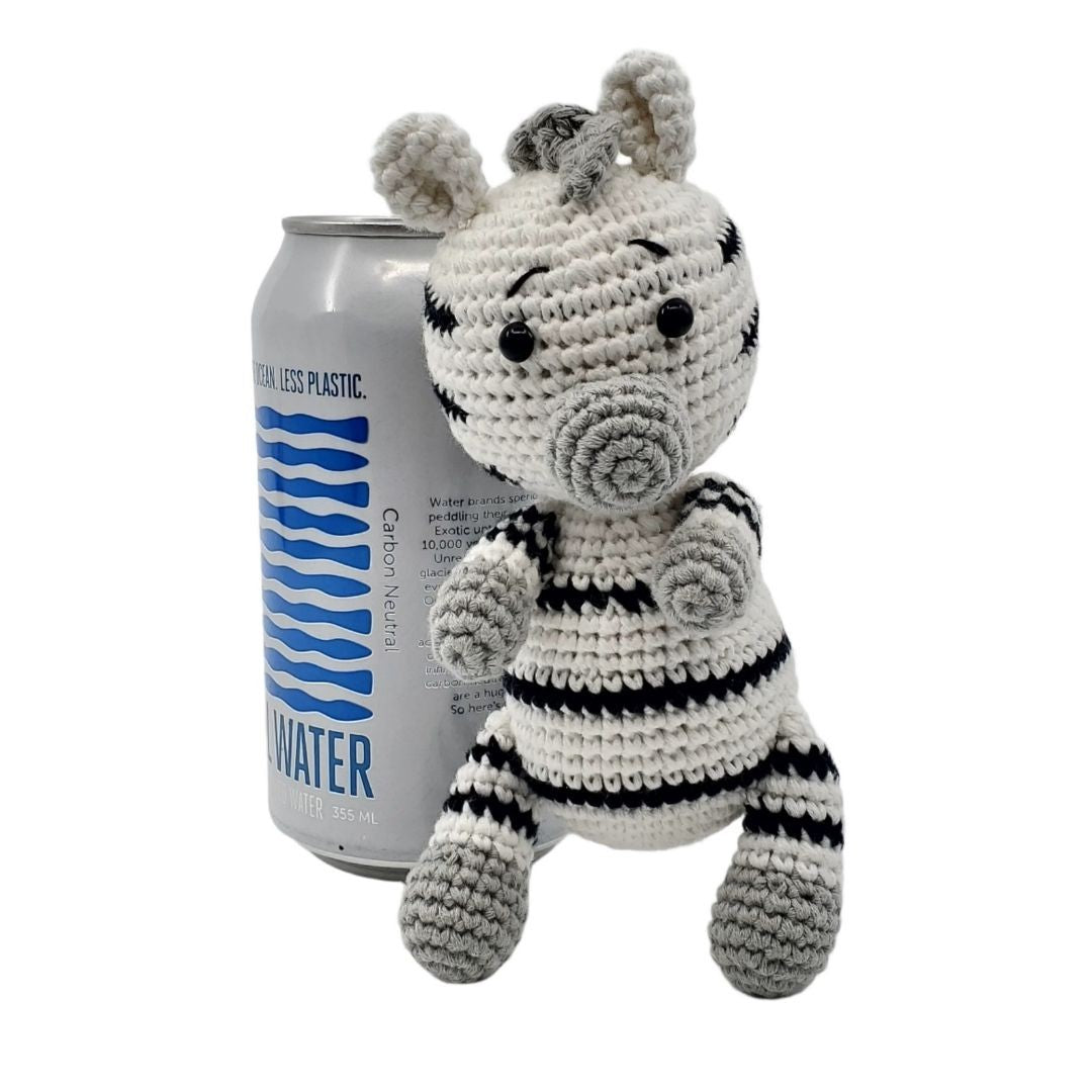 Crocheted zebra toy next to a can of water on a white background
